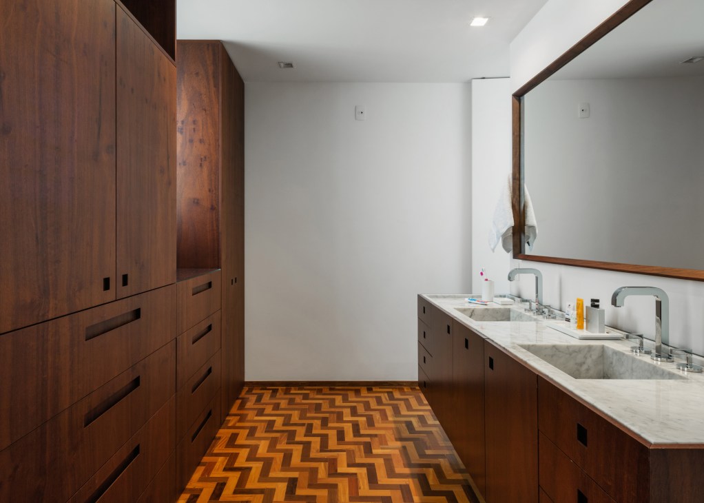 Modern bathroom with walnut cabinetry, marble countertop, double sinks, and herringbone wood flooring