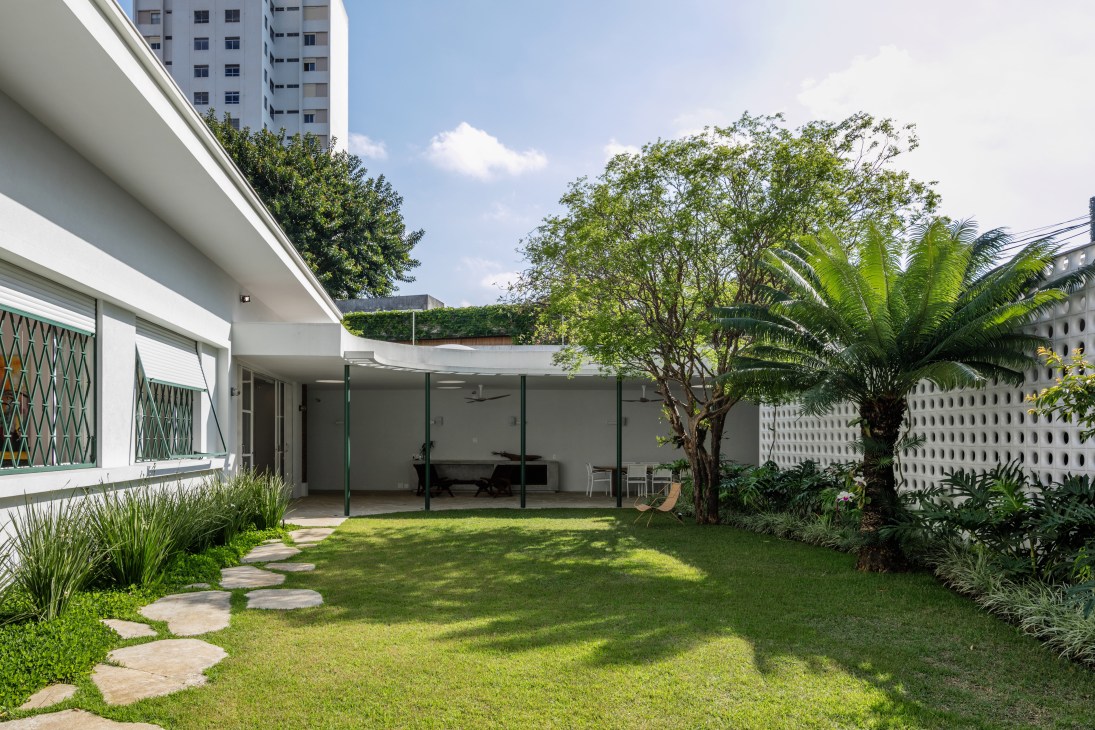 Modern white house with curved veranda overlooking lush green lawn and tropical garden with palm trees