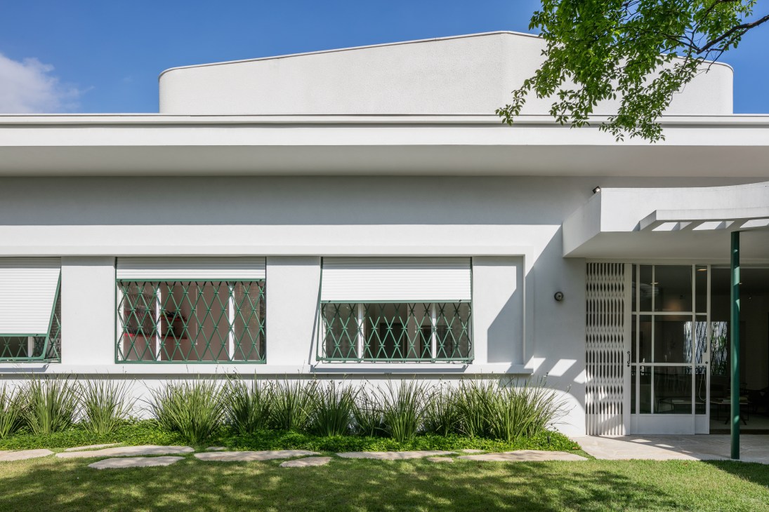 White modernist house facade with green diamond-patterned window grilles and landscaped front garden