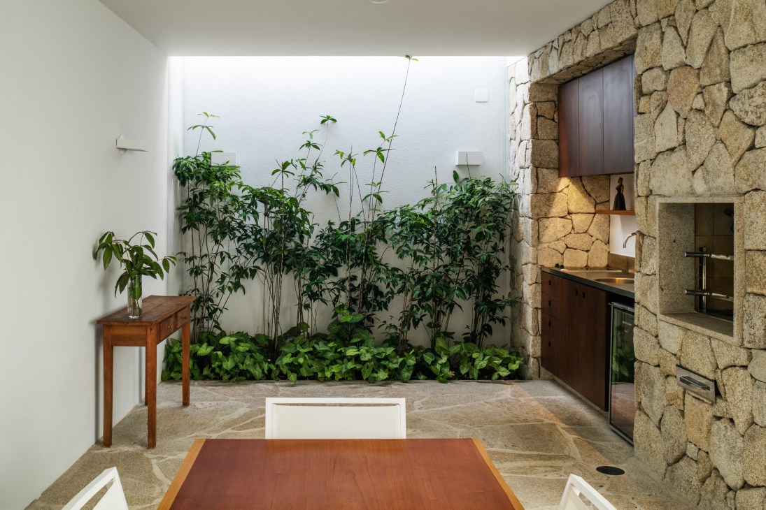 Stone barbecue area with built-in grill next to dining table and chairs in covered veranda