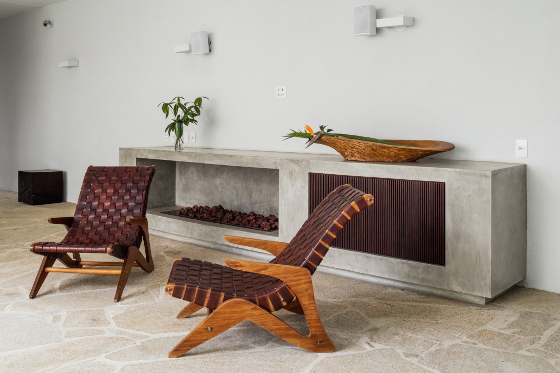 Concrete fireplace with woven leather chairs and wooden stool in minimalist interior