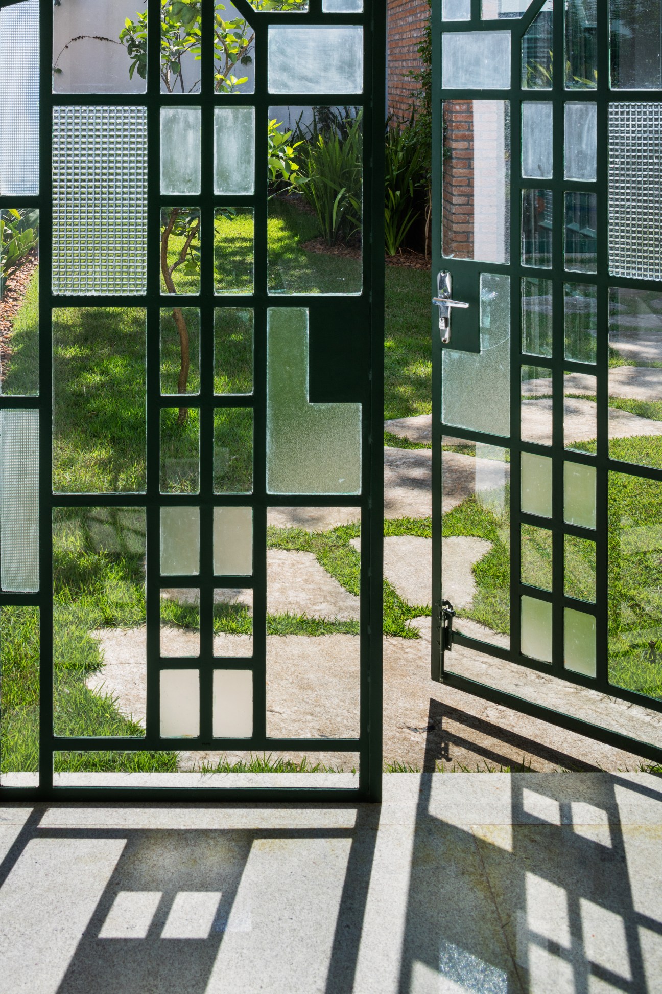 Green metal-framed windows with geometric glass panels overlooking garden pathway and lawn