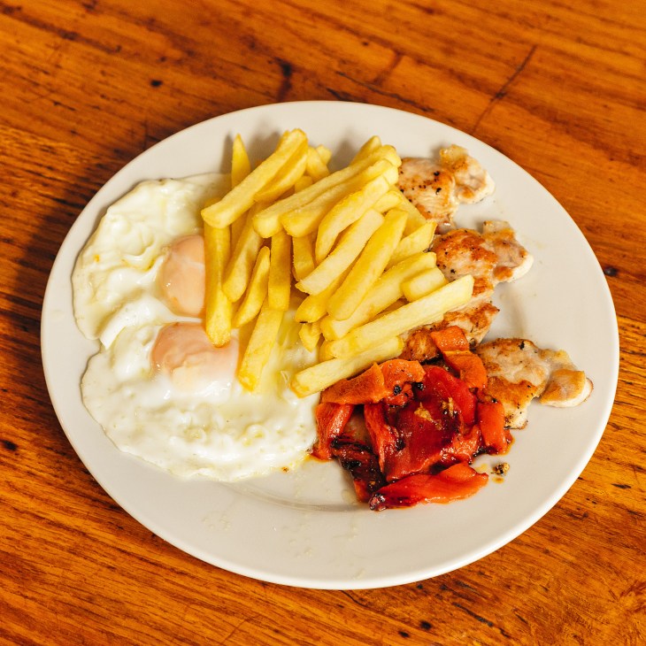 Fried egg with french fries and roasted red peppers on a white plate.
