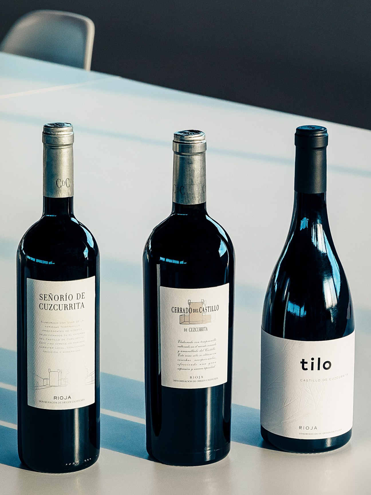 Three wine bottles from Castillo de Cuzcurrita winery displayed on a white table with mountains in background.