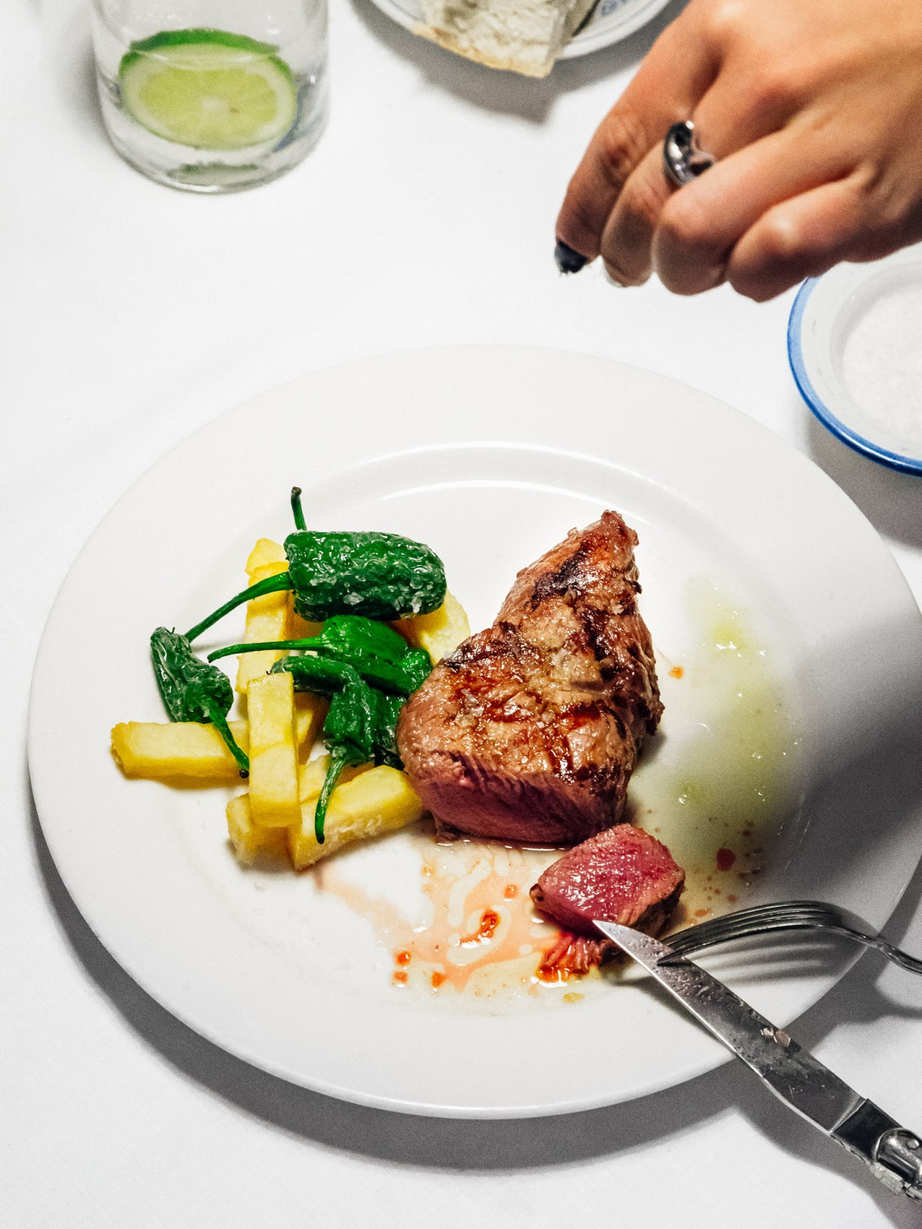 Seared steak with roasted peppers and chips on a white plate.