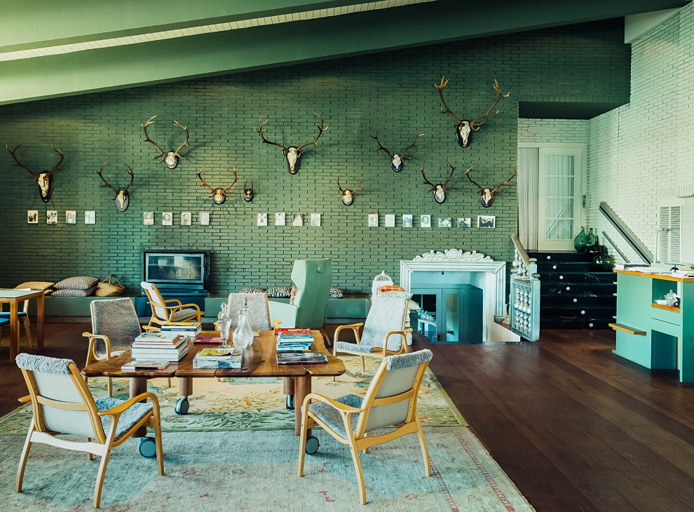 A mid-century modern lounge with sage green brick walls decorated with mounted deer heads, wooden furniture, and vintage decor.