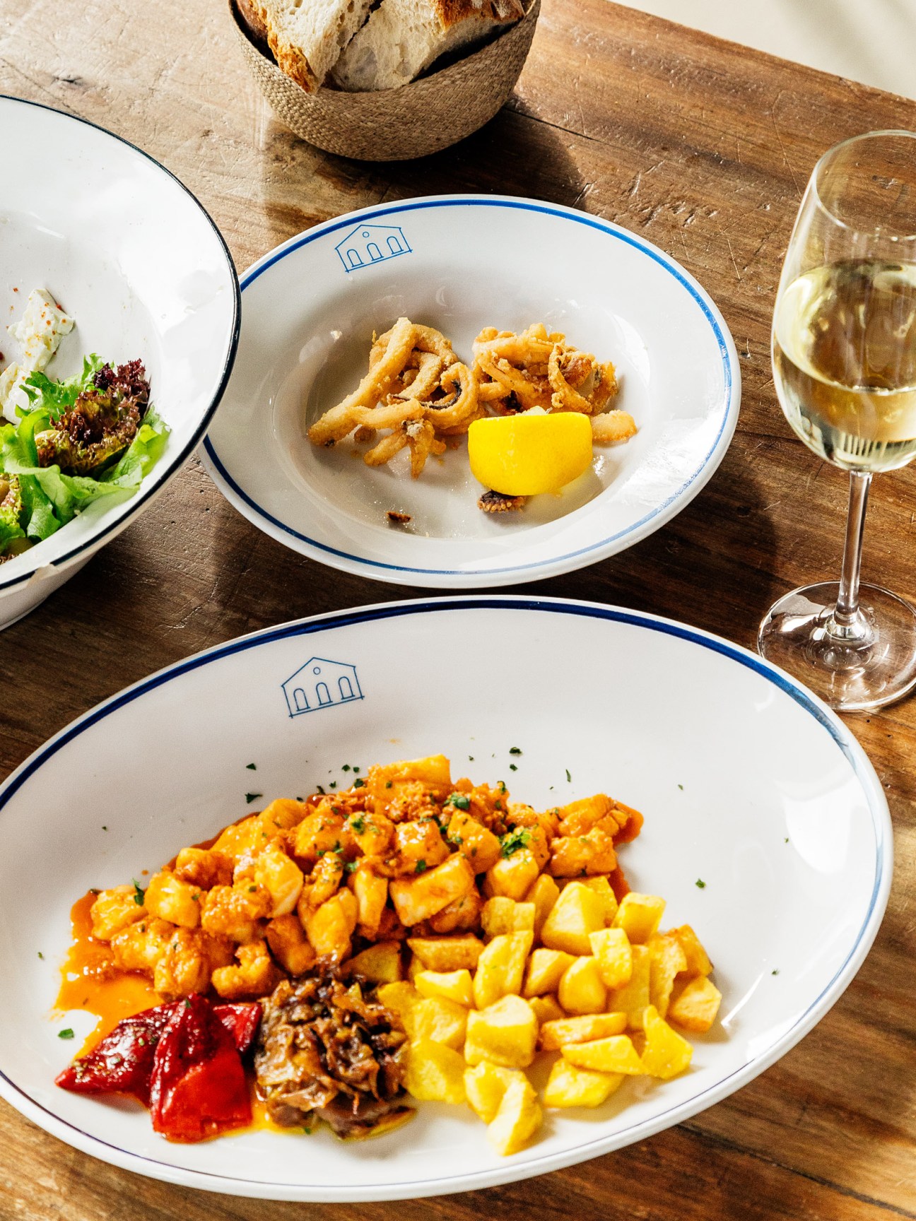 Plates of seafood and roasted potatoes on white bowls with blue trim at a restaurant table.