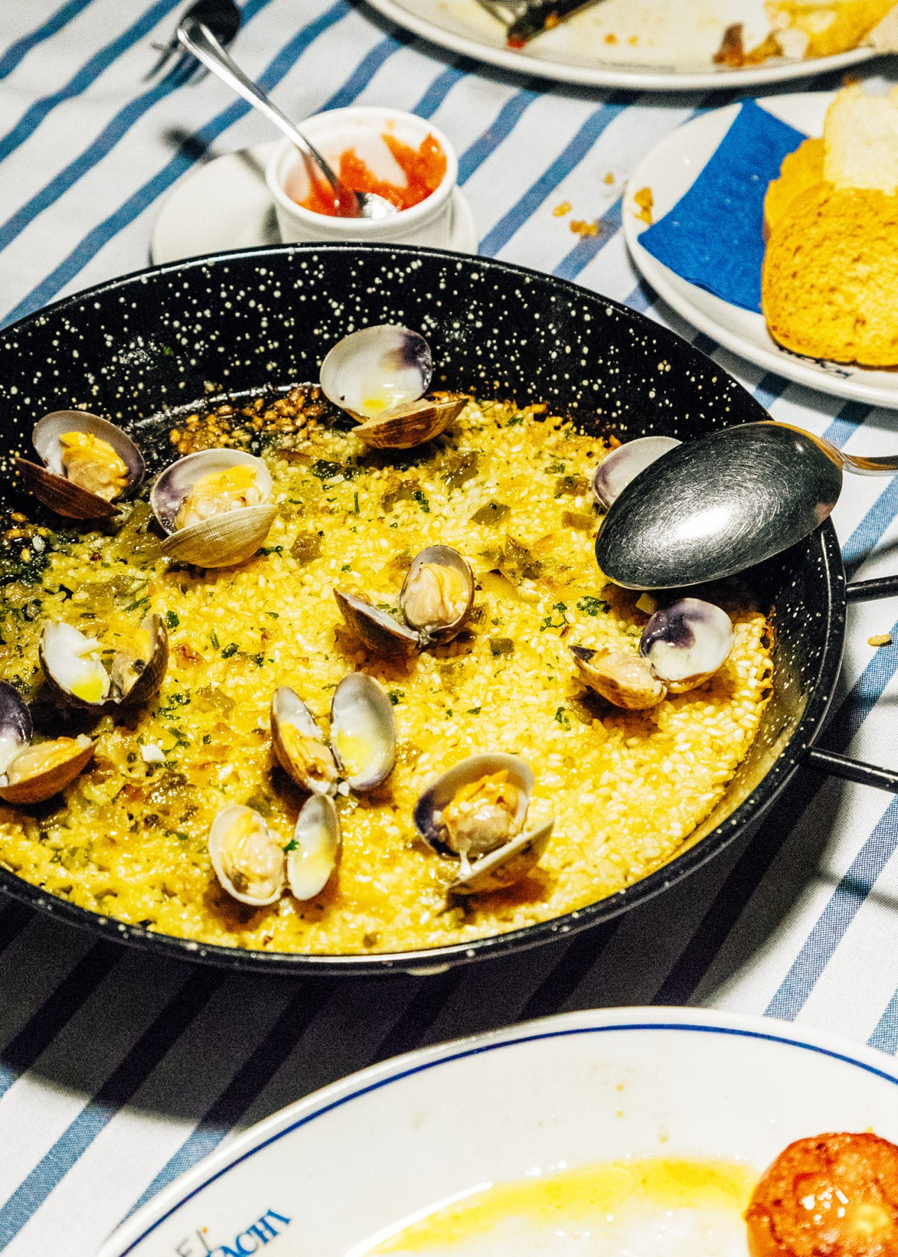 Seafood paella with clams in a black speckled pan on a striped tablecloth at El Machi restaurant.