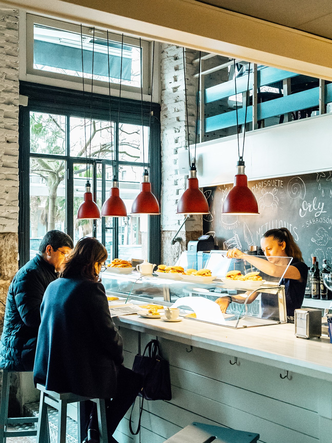 Customers ordering at El Machi's counter with red pendant lights and modern interior in Santander.