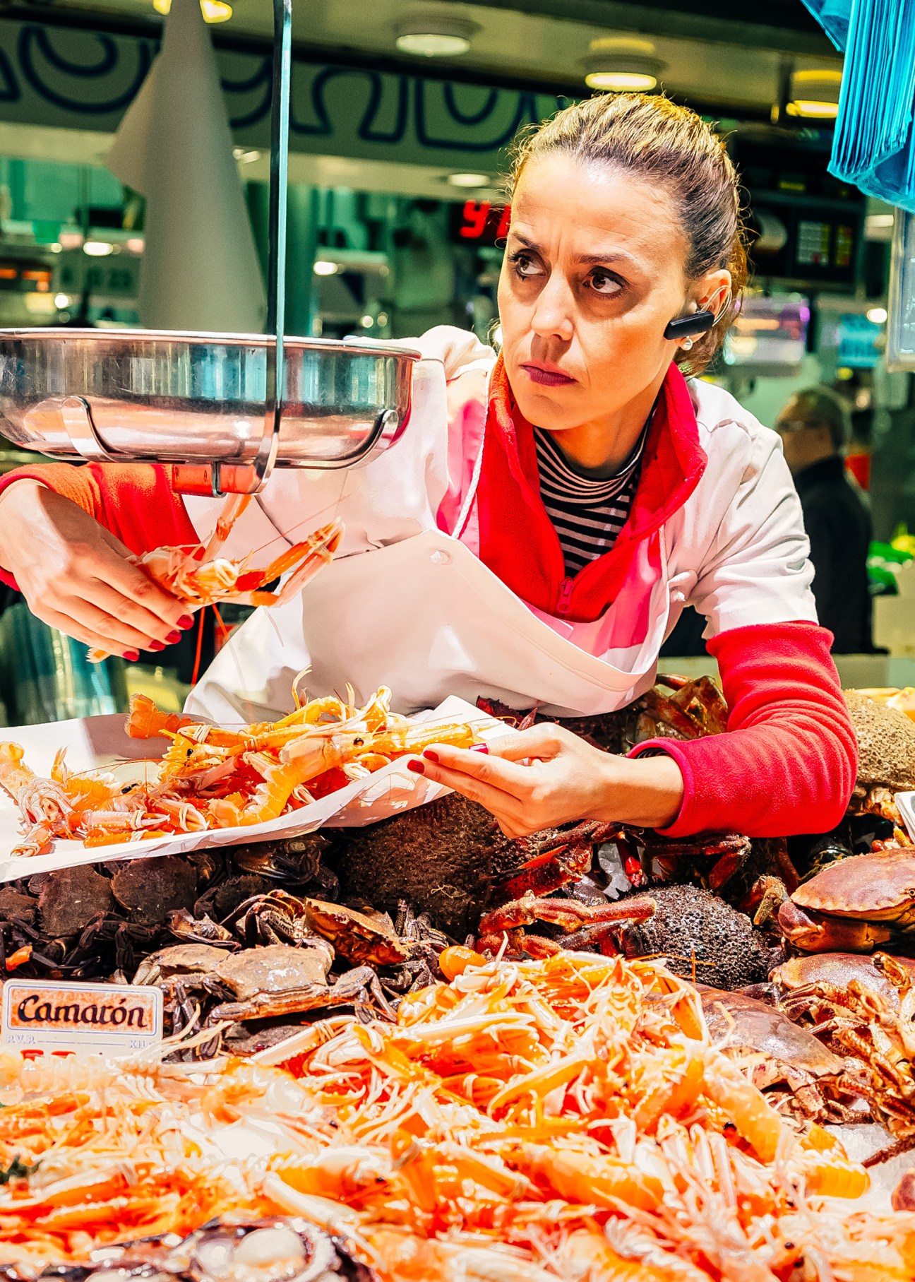 A woman in a white coat and red scarf sells fresh orange shrimp at Santander's La Esperanza seafood market.