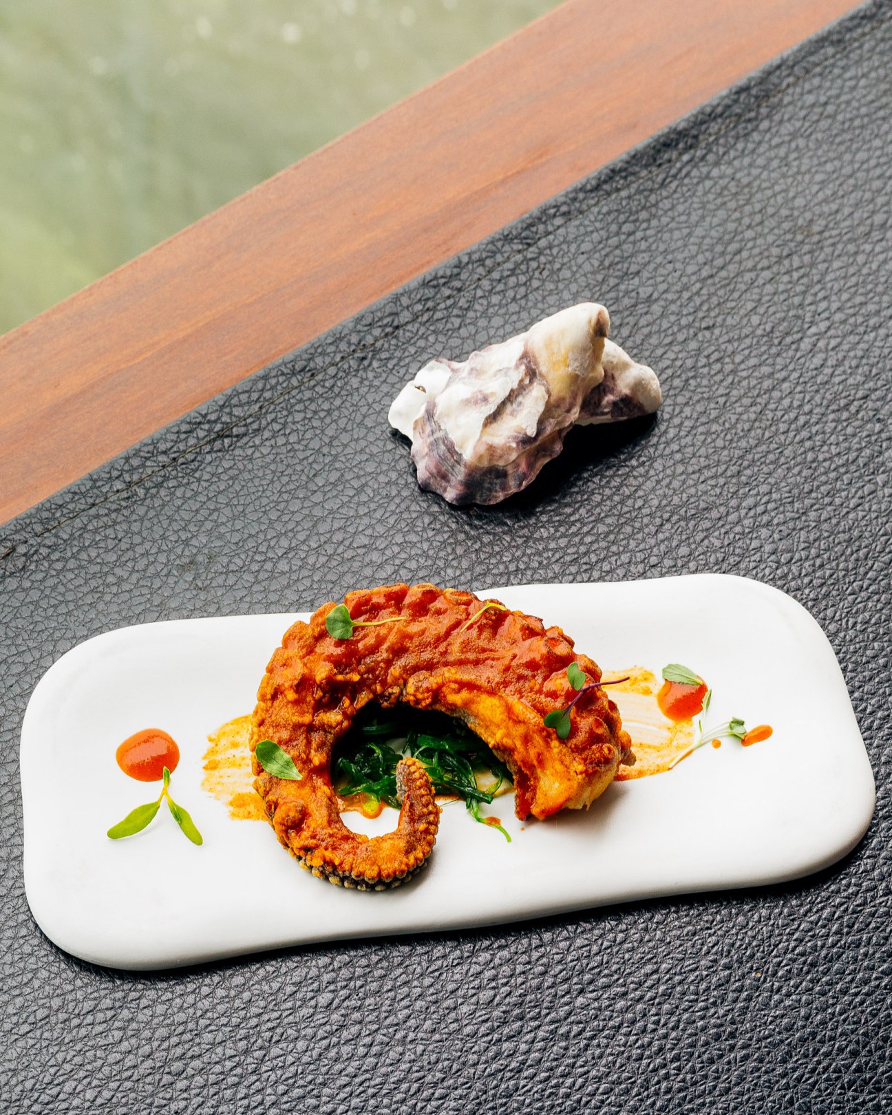 Crispy fried octopus tentacle with green garnish on white plate at Annua restaurant.