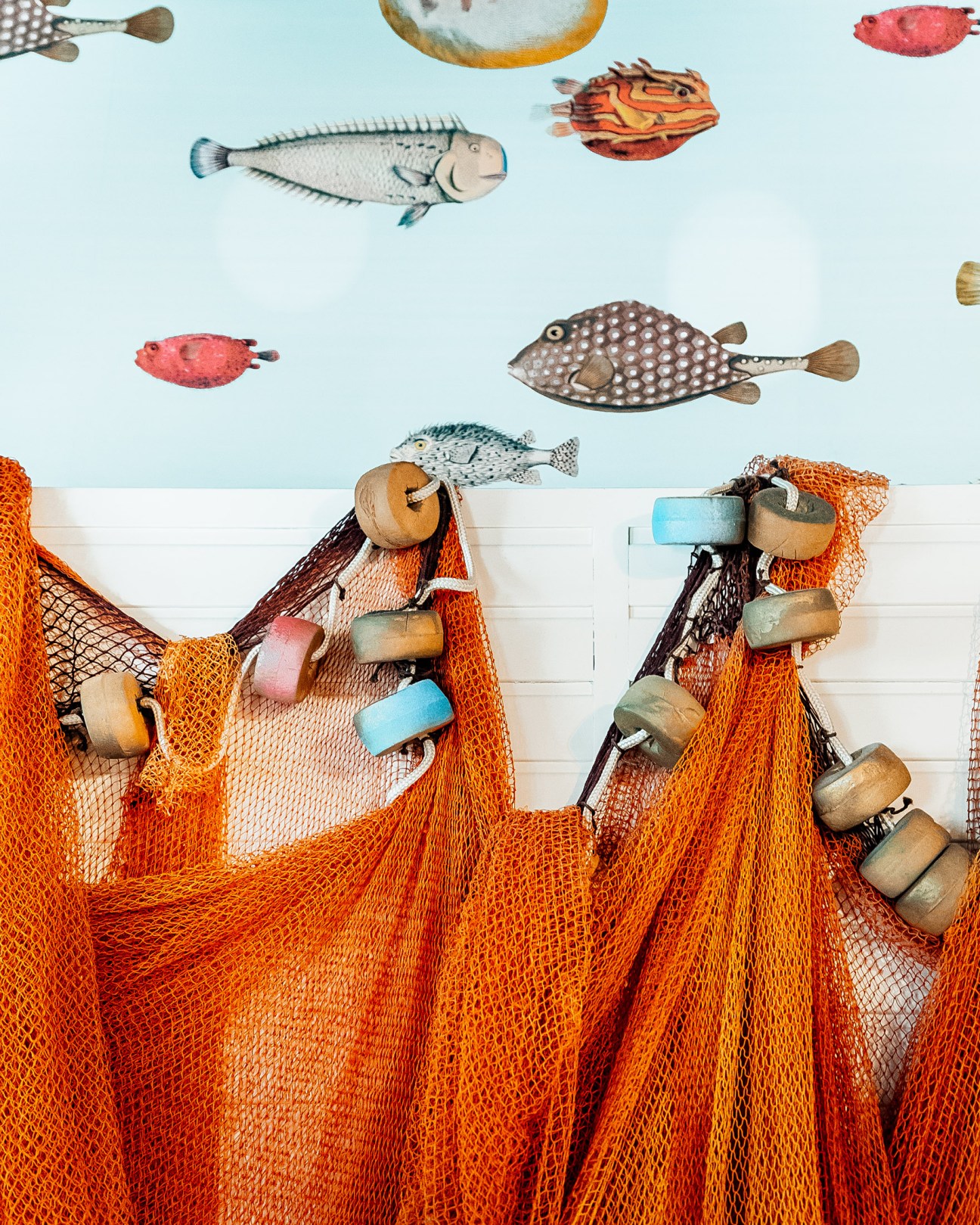 Fishing nets with wooden floats and painted fish illustrations on a wall.