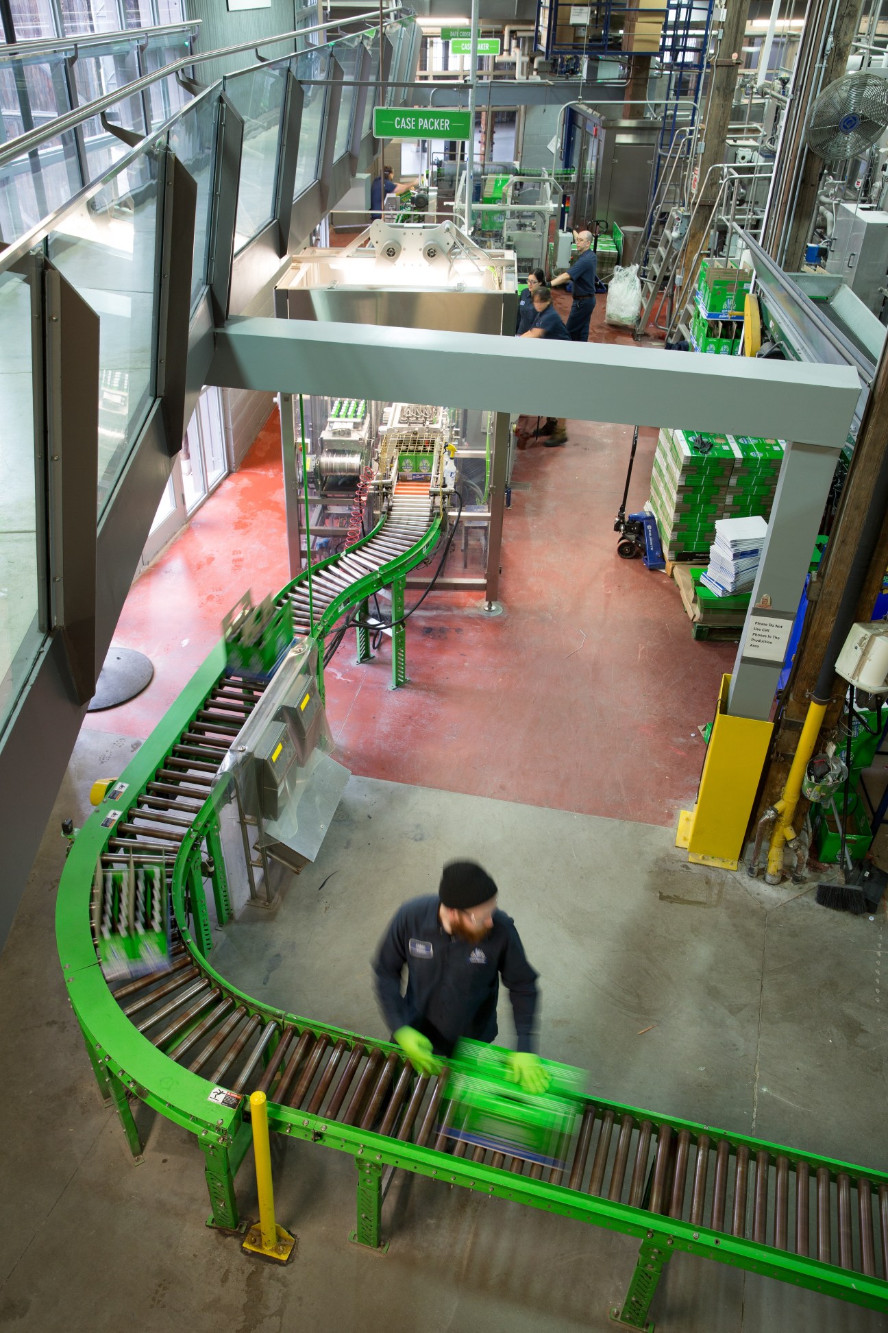 Overhead view of a green conveyor belt packaging line at a brewery facility with workers and equipment.
