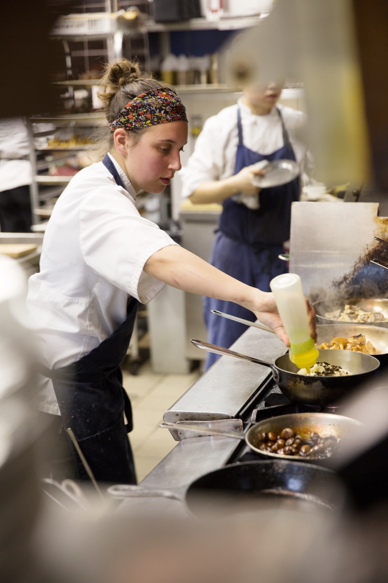 Chef in white jacket and colorful headband cooking at Splendido's kitchen stove with colleagues working in background.