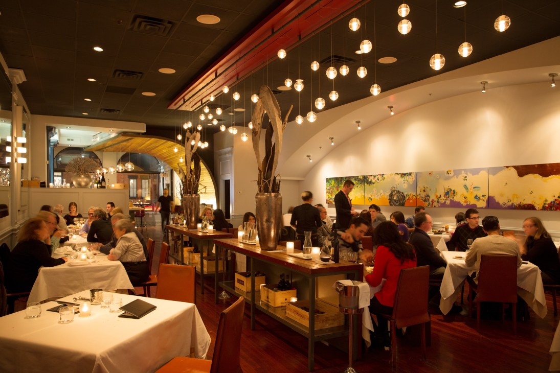 Fine dining room at Splendido restaurant with diners seated at tables under hanging pendant lights.