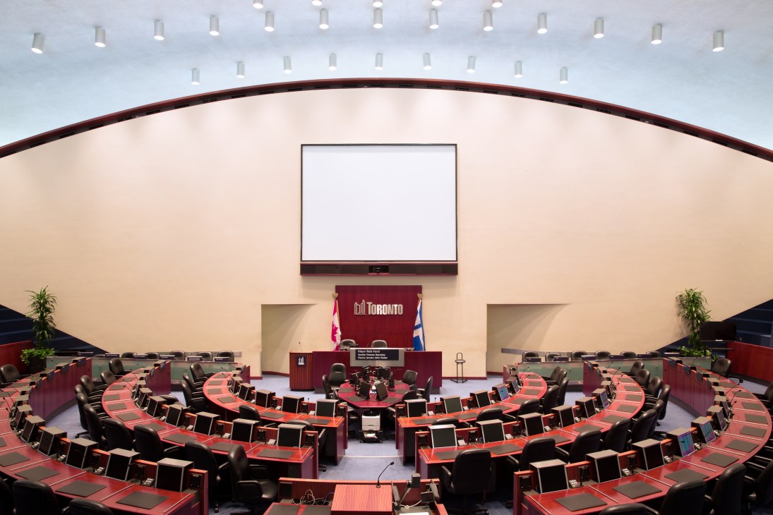 Toronto City Hall's council chamber with curved seating, red desks, and distinctive domed ceiling with skylights.