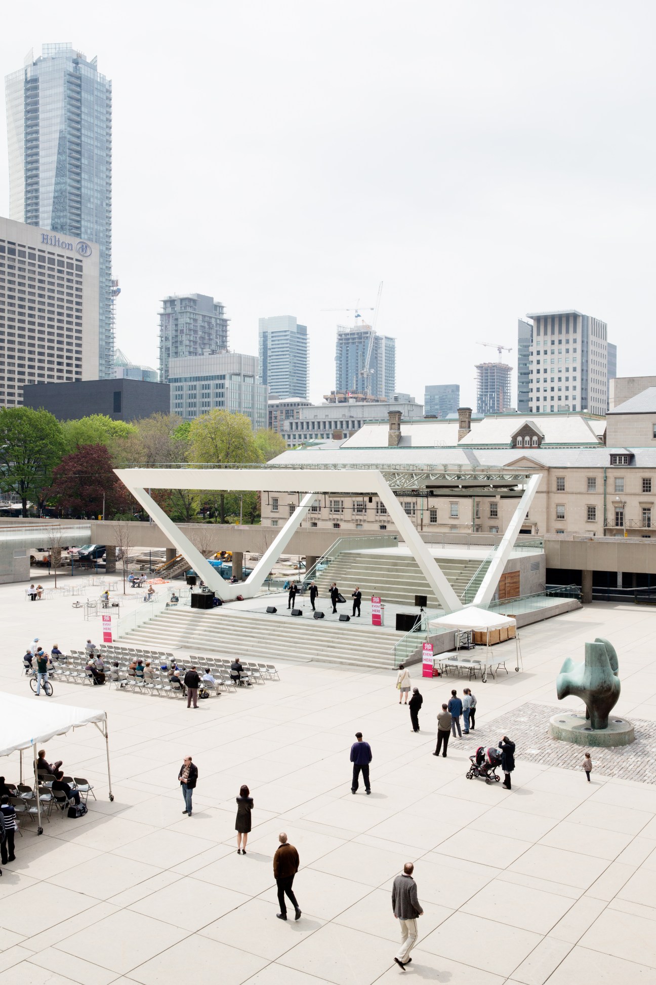 People gathered in Nathan Phillips Square during a lunchtime performance with Toronto's modernist City Hall and skyline in background.