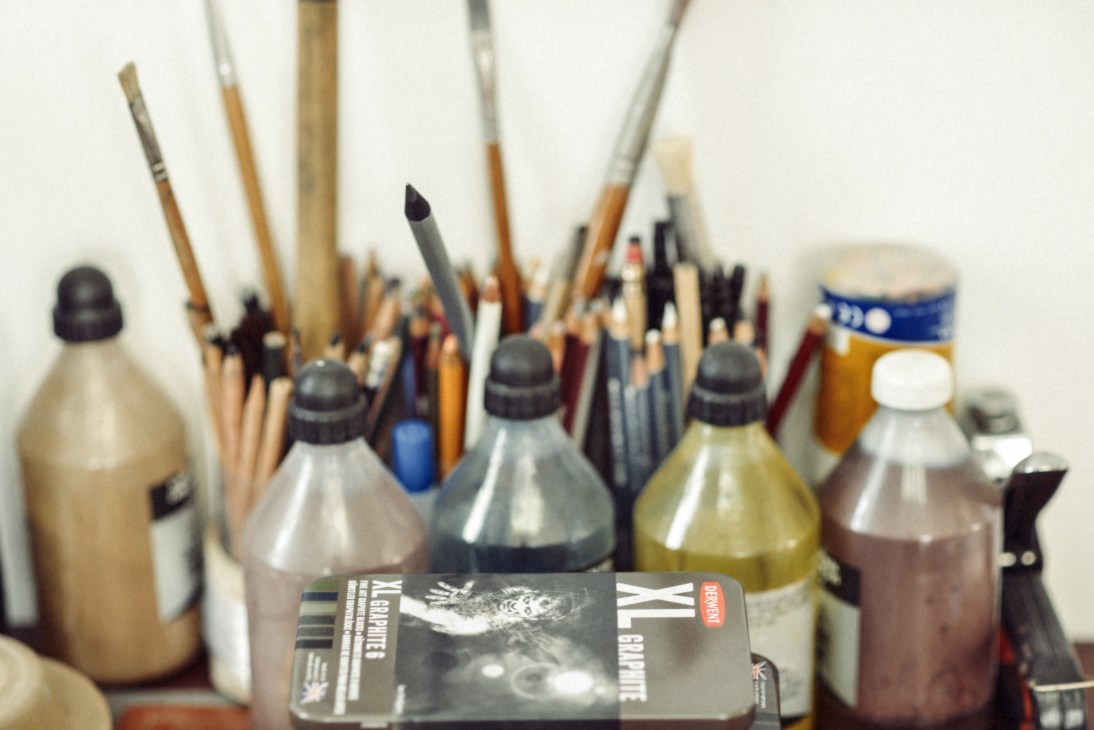 Paintbrushes and bottles of paint and ink arranged on a studio workspace.