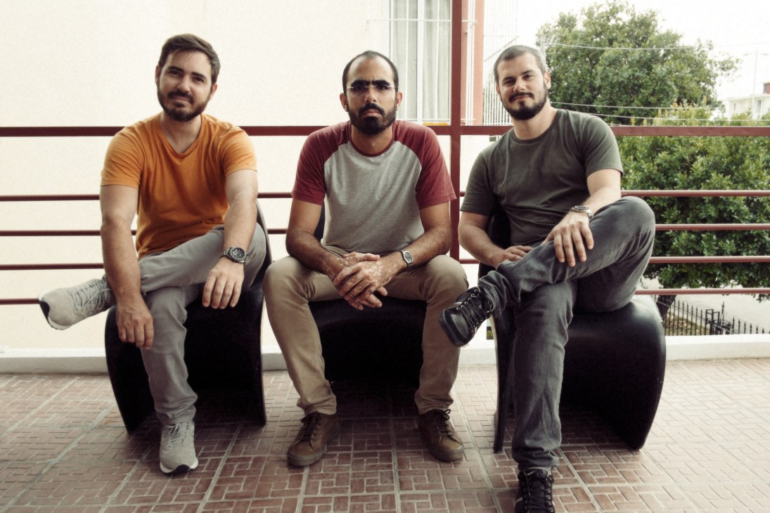 Three male artists sitting on a bench outdoors in casual clothing