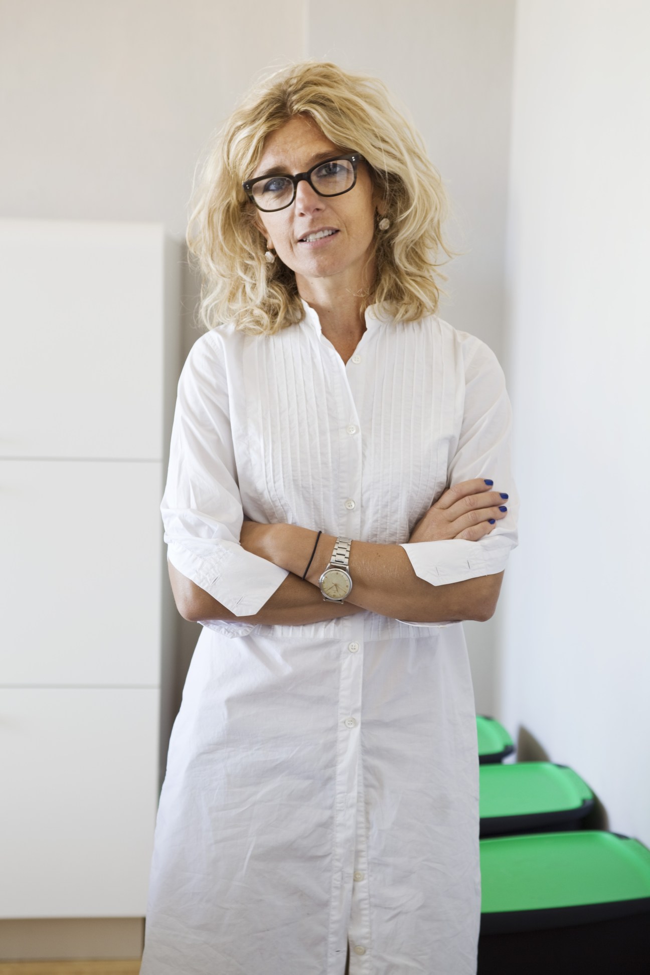 Architect Paola Sausa wearing glasses and white shirt, arms crossed, smiling at camera.