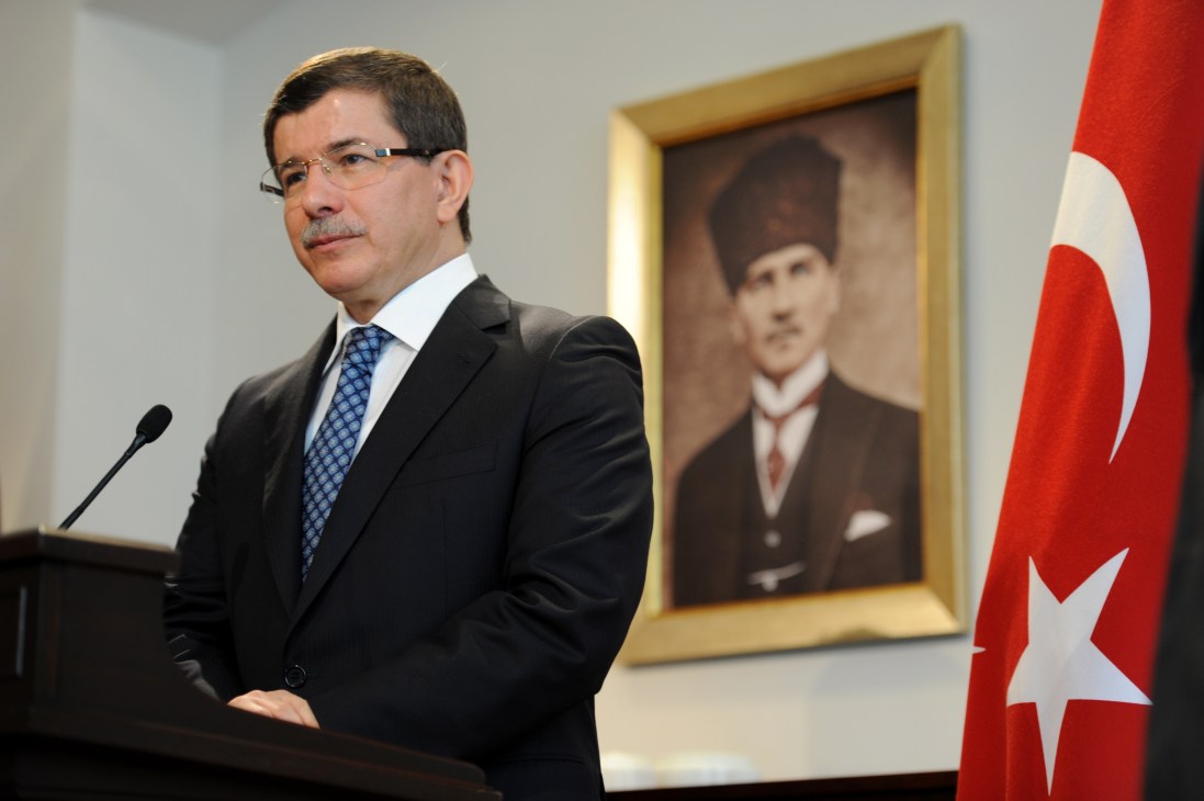 Ahmet Davutoglu, Turkey's foreign minister, stands at a podium with a Turkish flag and portrait in the background.