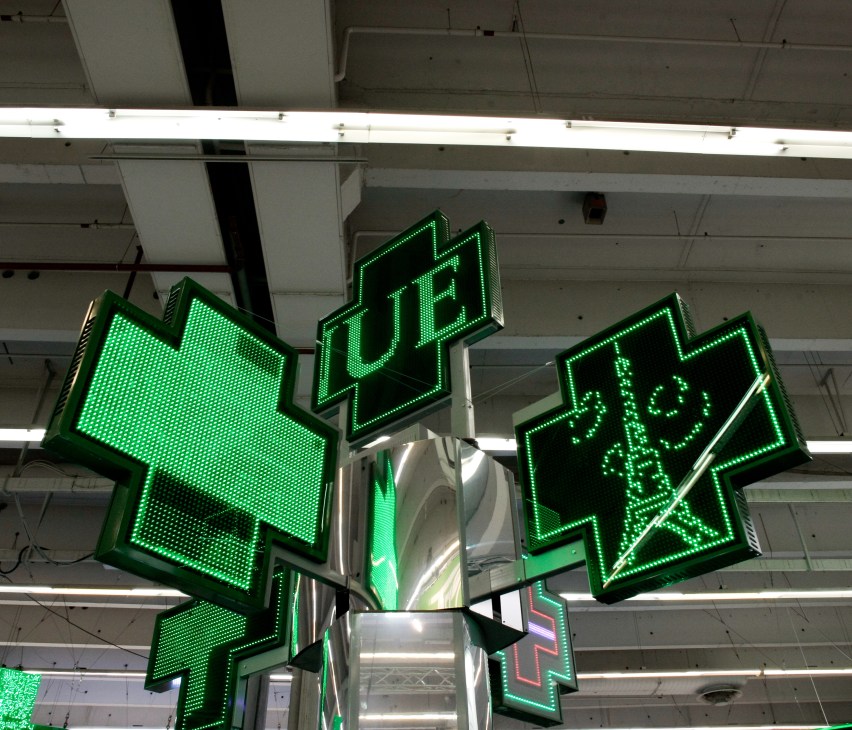 Green neon pharmacy cross signs hanging from ceiling in exhibition space