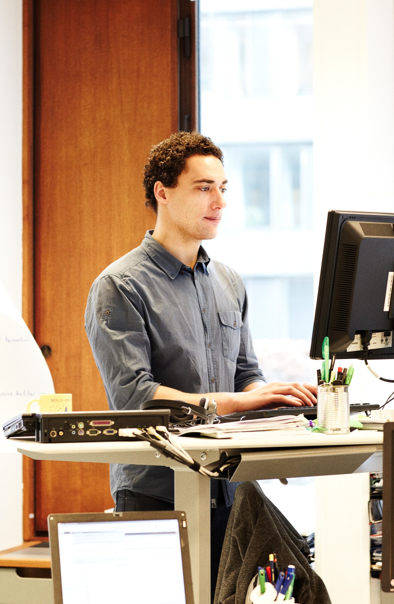 Jesper Christiansen, a business PhD and anthropologist, works at a desk with a computer in a bright office space with wooden paneling.