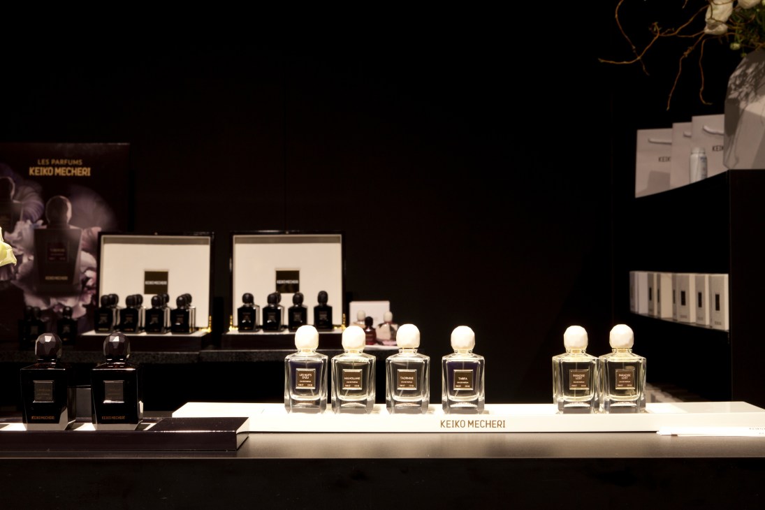Keiko Mecheri perfume stand displaying bottles with white sphere caps at a trade fair.