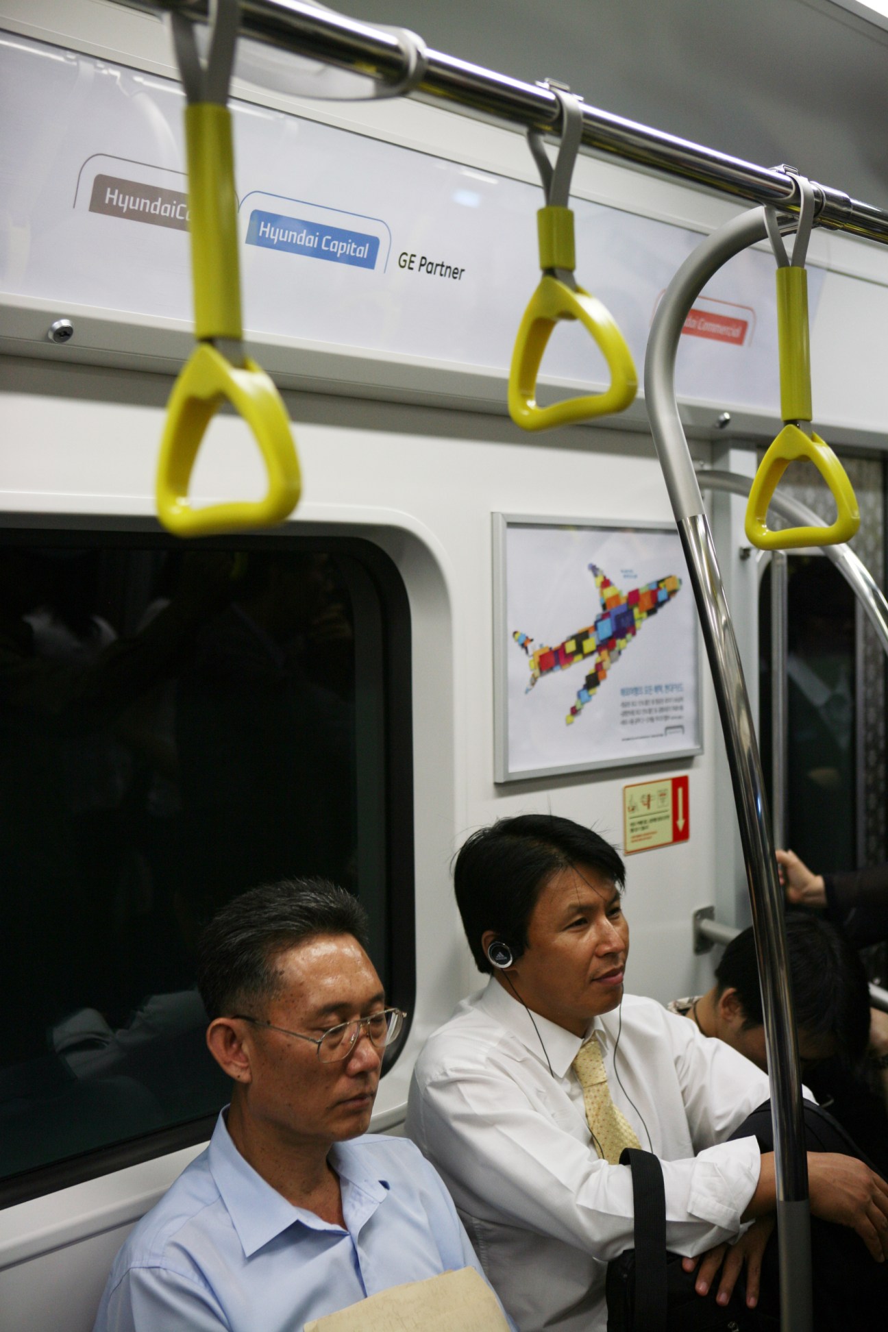 South Korean commuters sit inside a Seoul Line 9 subway car with Hyundai Capital advertising visible above.