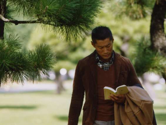 Man reading under pine trees wearing Traditional Weatherwear jacket, United Arrows jumper, and Biesot duffle coat.