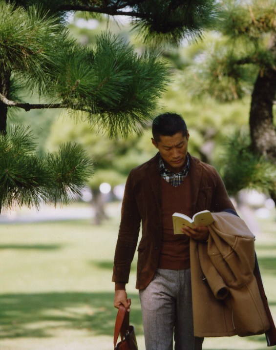Man reading under pine trees wearing Traditional Weatherwear jacket, United Arrows jumper, and Biesot duffle coat.