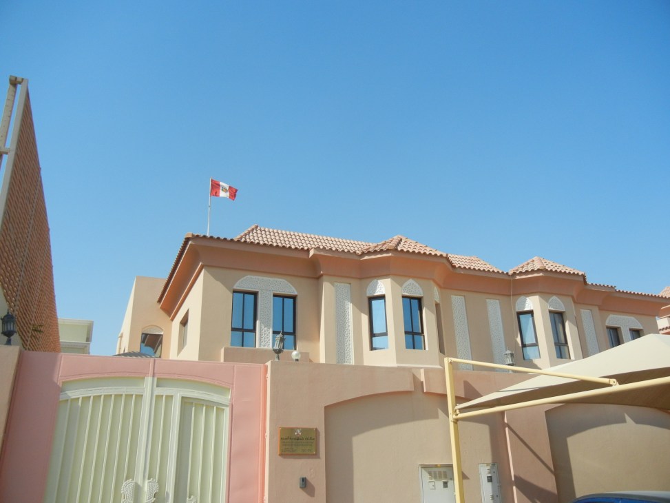Peruvian embassy building in the Middle East with national flag flying above tan-colored facade.
