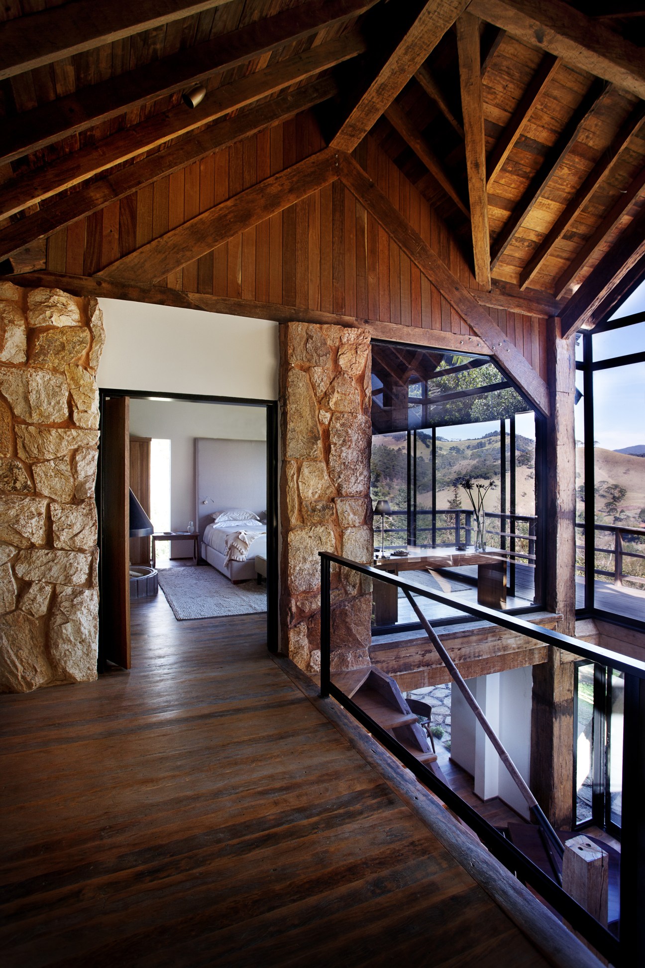 Interior of Botanique Hotel villa with wooden beams, stone walls, and floor-to-ceiling windows overlooking rainforest.