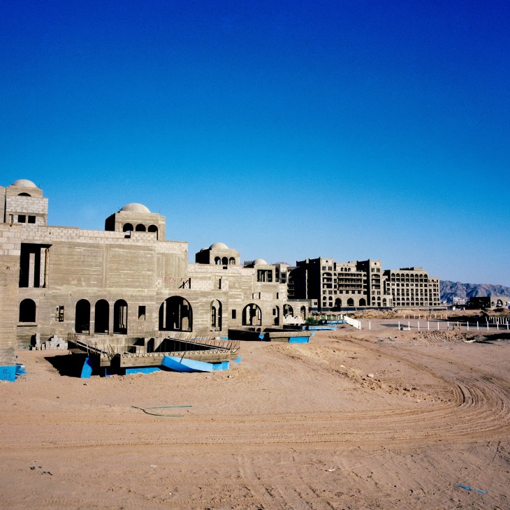 Beachfront construction site showing stone villas with domed roofs at Saraya Aqaba development project with mountains in background.