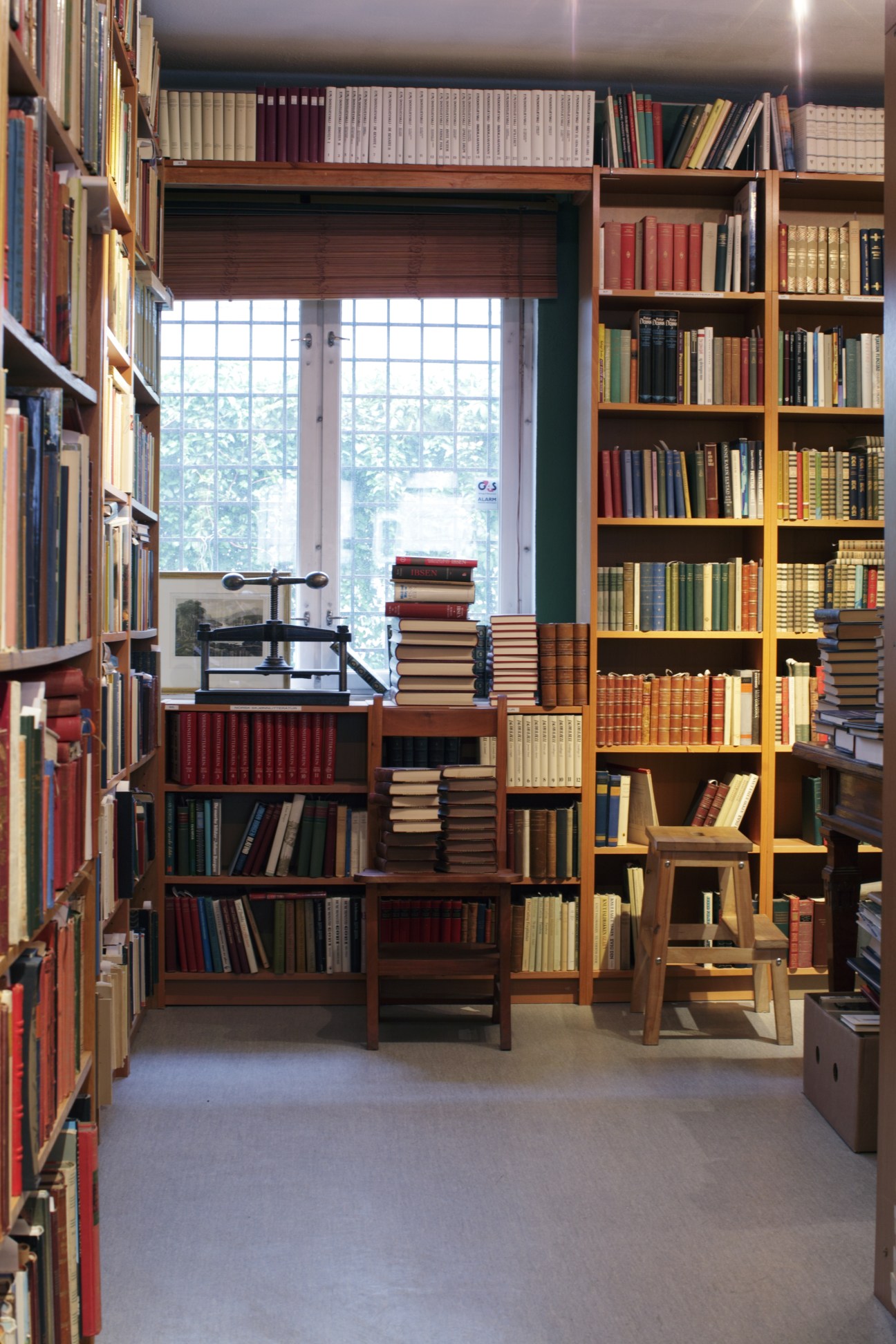 Interior of Adamstuen Antikvariat bookshop with wooden shelves filled with old books, a desk with scale, and large windows overlooking the street.