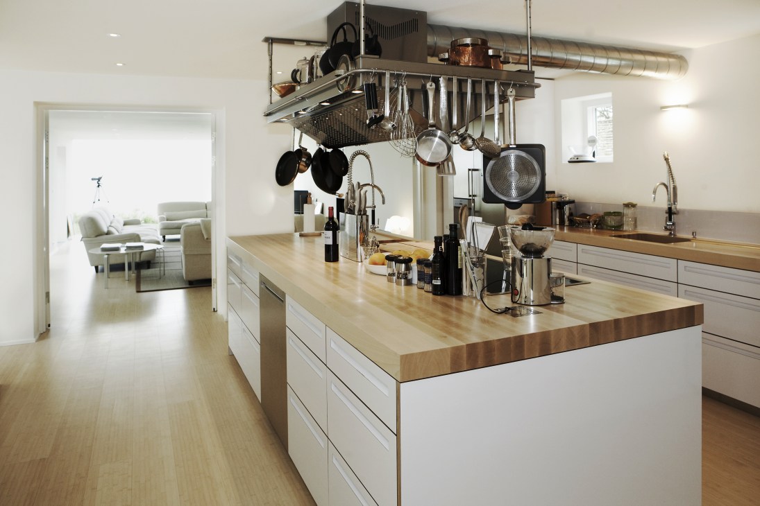 Modern kitchen with white cabinetry, wooden countertop, and stainless steel hanging rack with kitchenware and utensils.