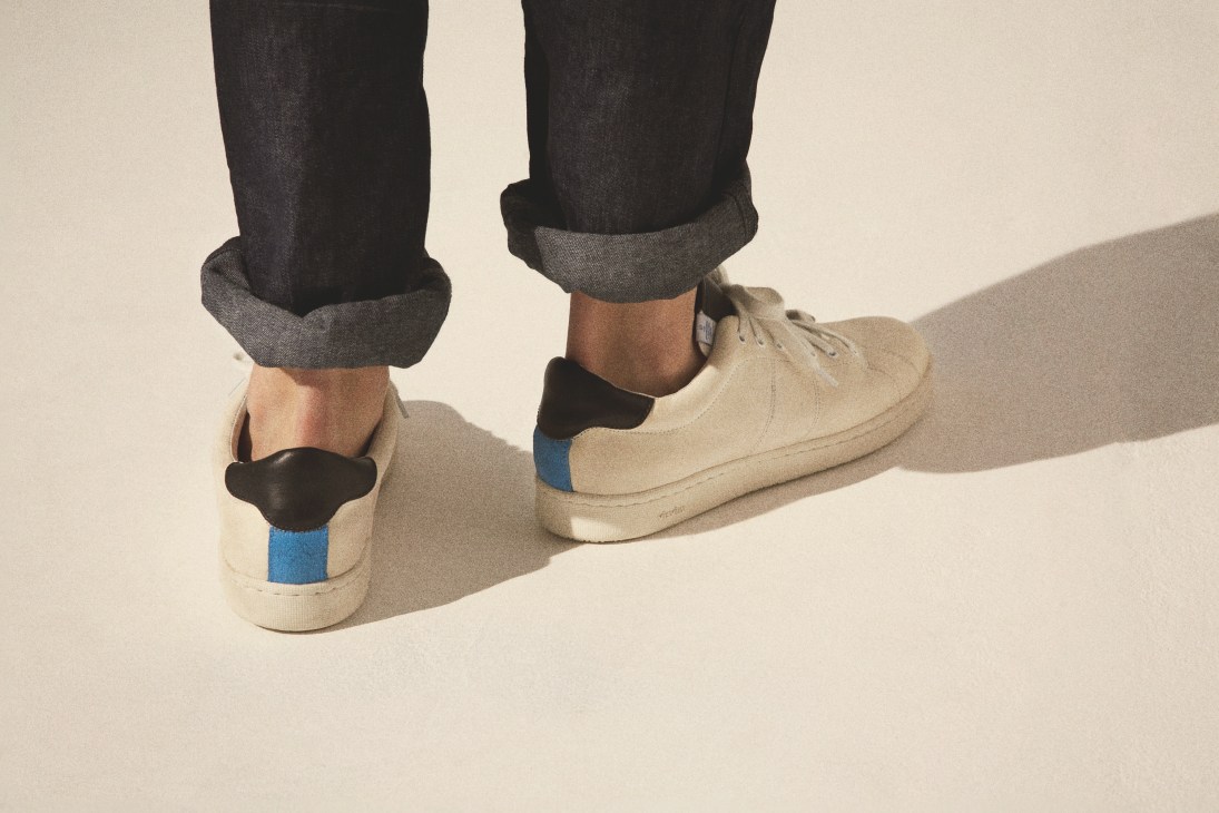 Person wearing cream Visvim Foley GY FOLK shoes with blue stripe detail and dark cuffed pants.