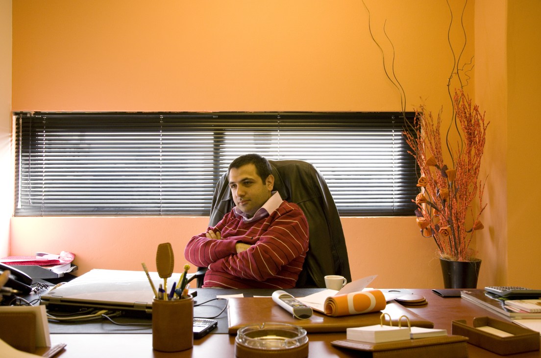 Chadi el Hachem, PR manager of OTV, sitting at his desk in an office with orange walls and horizontal blinds.