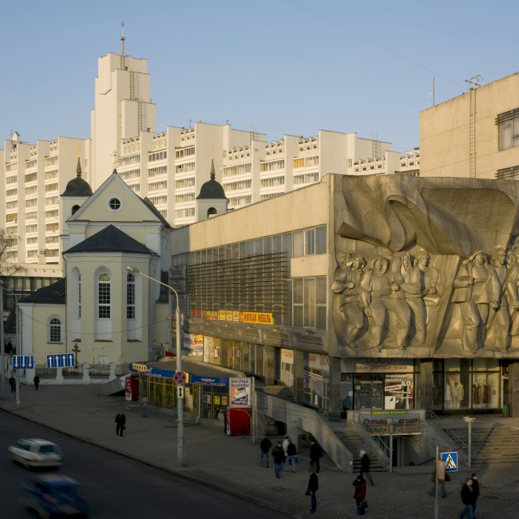 Soviet-era stone relief sculpture of figures on building facade in central Minsk surrounded by Stalinist architecture.