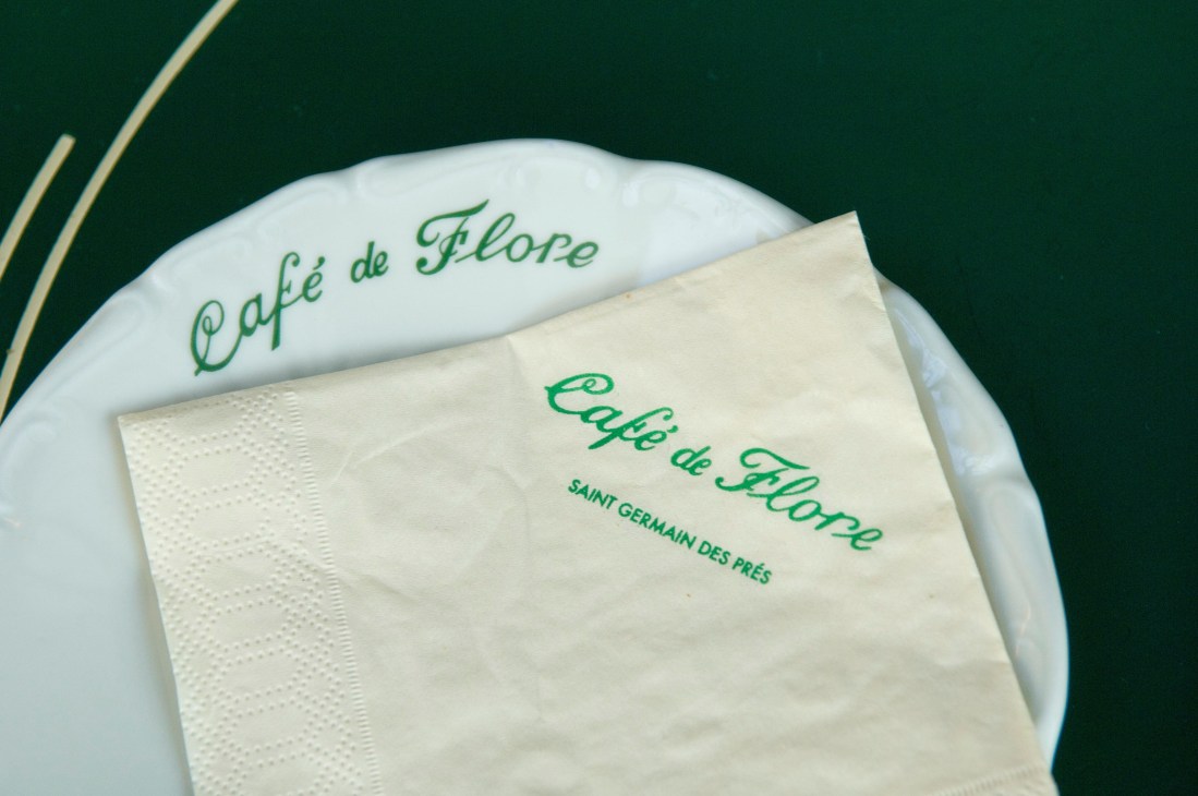 Café de Flore branded napkin and plate on green background.