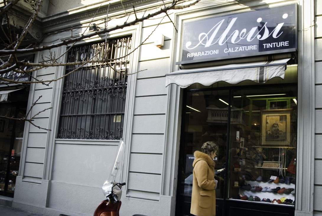 Storefront of Alvisi shoe repair shop in Milan displaying signage for shoe repairs, dyeing and polishing services.