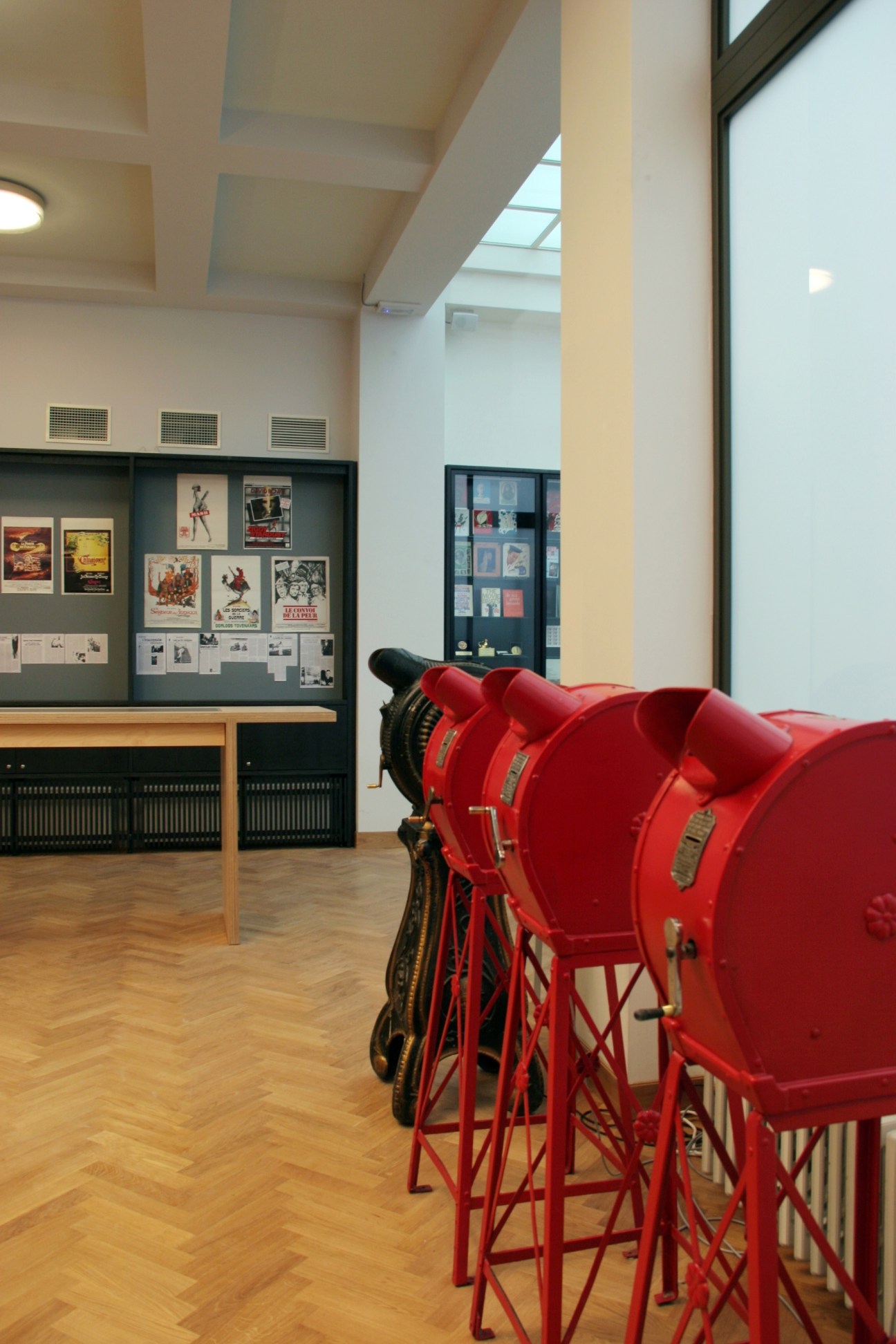 Interior of Cinematek film museum showing vintage red film projectors and exhibition displays with movie posters.
