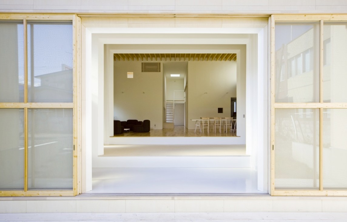 Minimalist interior space in Hokkaido with light wood frames, white walls, and sparse furnishings visible through open glass doors.