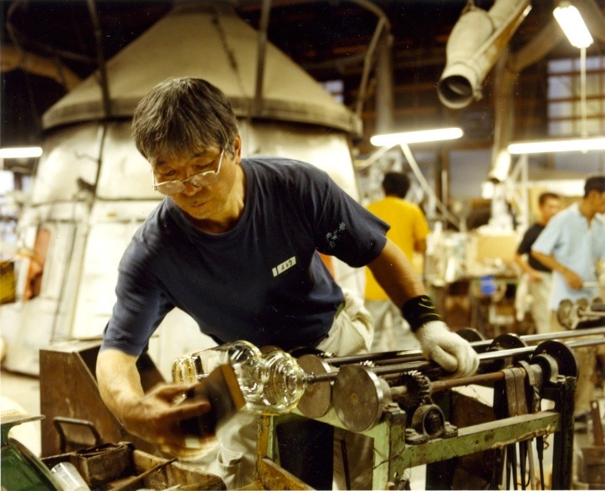 Glass blower in protective eyewear inspects a hand-blown glass at Shotoku factory in Tokyo.