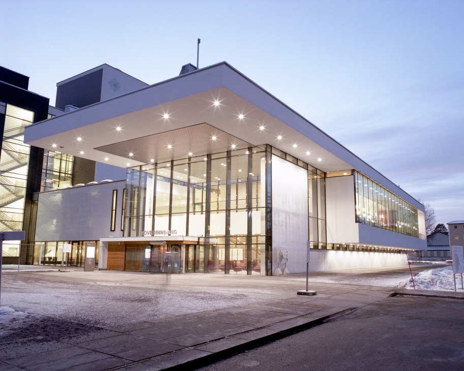 Akershus University Hospital front entrance at dusk with illuminated glass facade and modern architectural design.