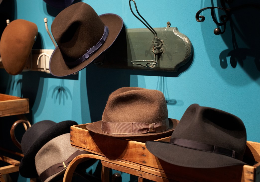 Display of various Borsalino hats in different styles and colors on wooden stands against a bright blue background.