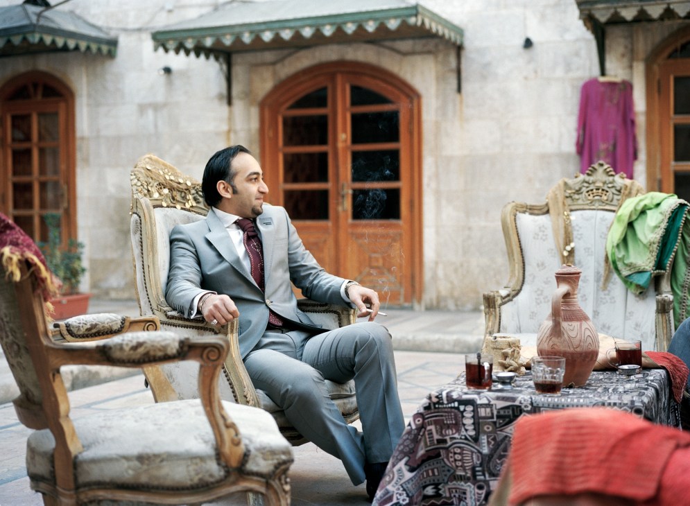 Mazen Salah, a man in a grey suit and burgundy tie, sits in an ornate chair in a courtyard with traditional architecture and wooden doors.