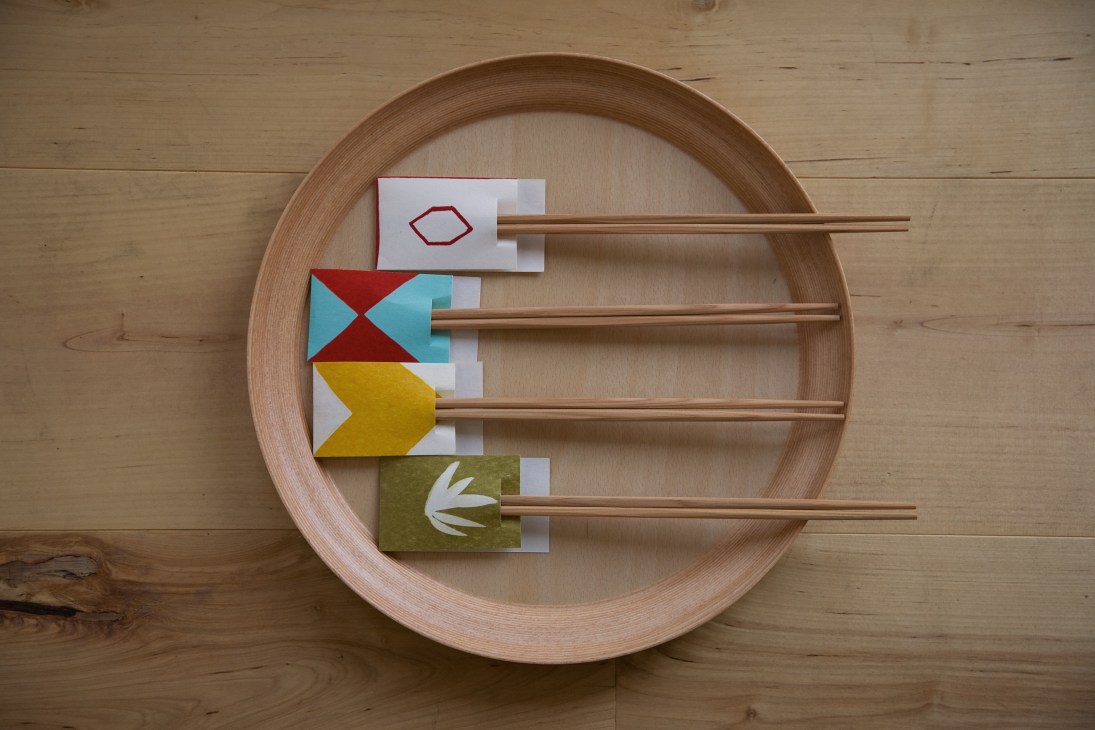 Wooden chopsticks with colorful patterned rest holders arranged on a round wooden plate.