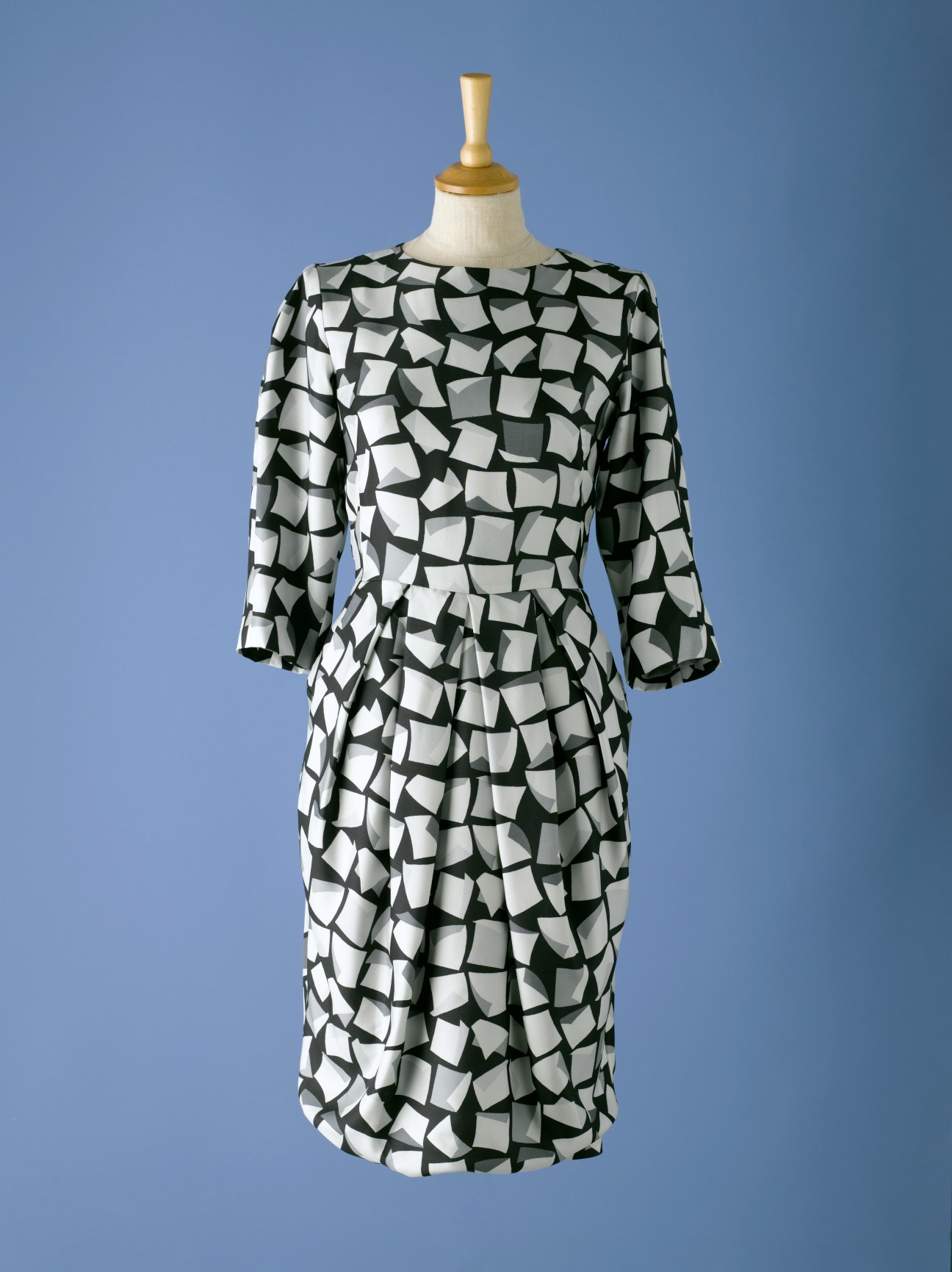Black and white geometric patterned three-quarter sleeve dress on mannequin against blue background.