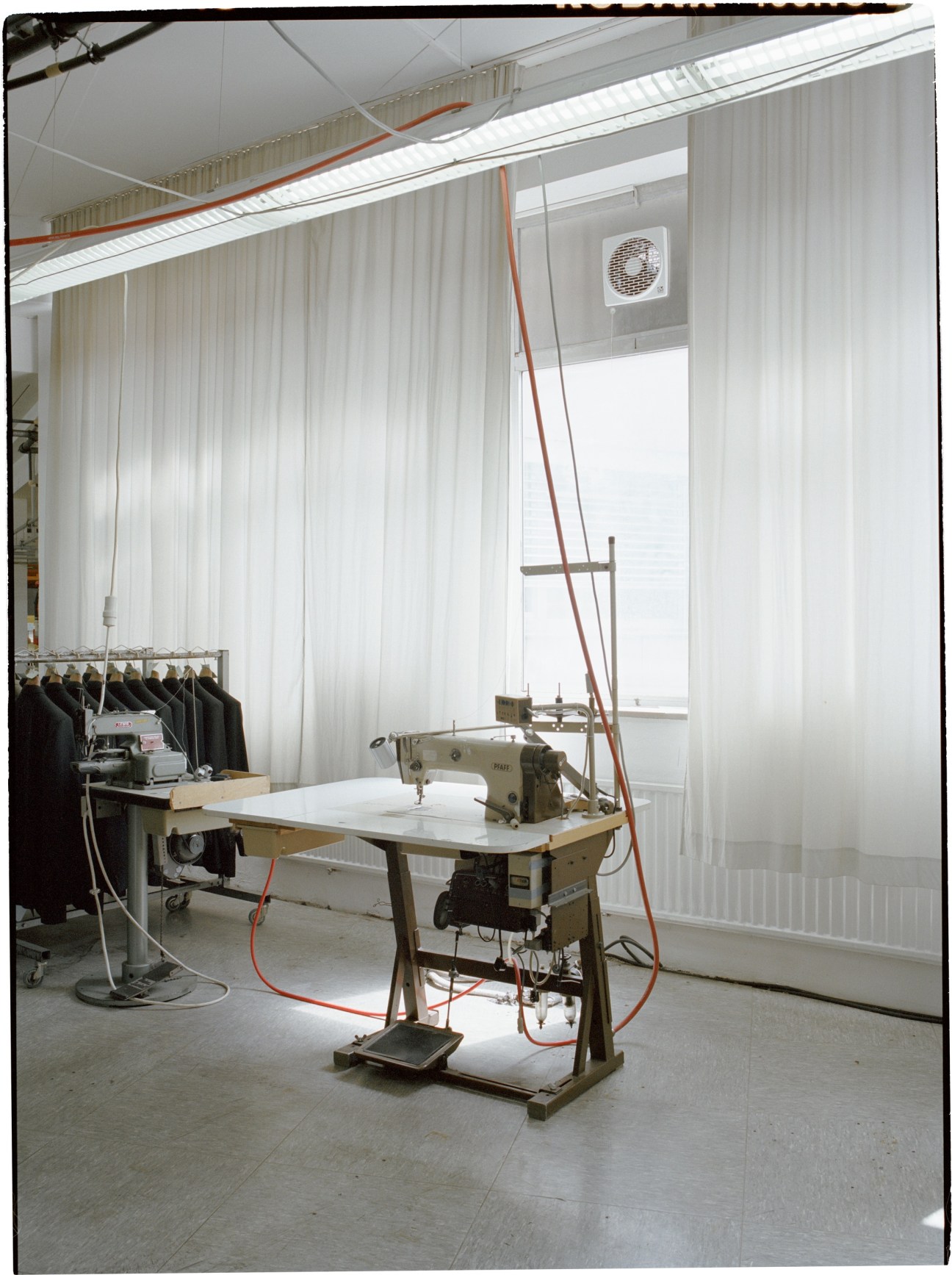 Vintage Pfaff sewing machine in a bright atelier space with clothing racks and red cables.